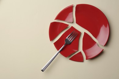 Pieces of broken red ceramic plate and fork on beige background, top view. Space for text