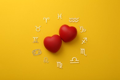 Photo of Zodiac signs and red hearts on yellow background, flat lay