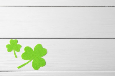 St. Patrick's day. Decorative green clover leaves on white wooden table, flat lay. Space for text