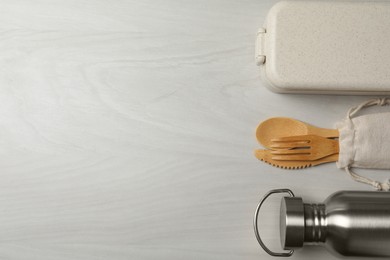 Photo of Lunch box, metal bottle and bamboo cutlery on white wooden table, flat lay with space for text. Conscious consumption