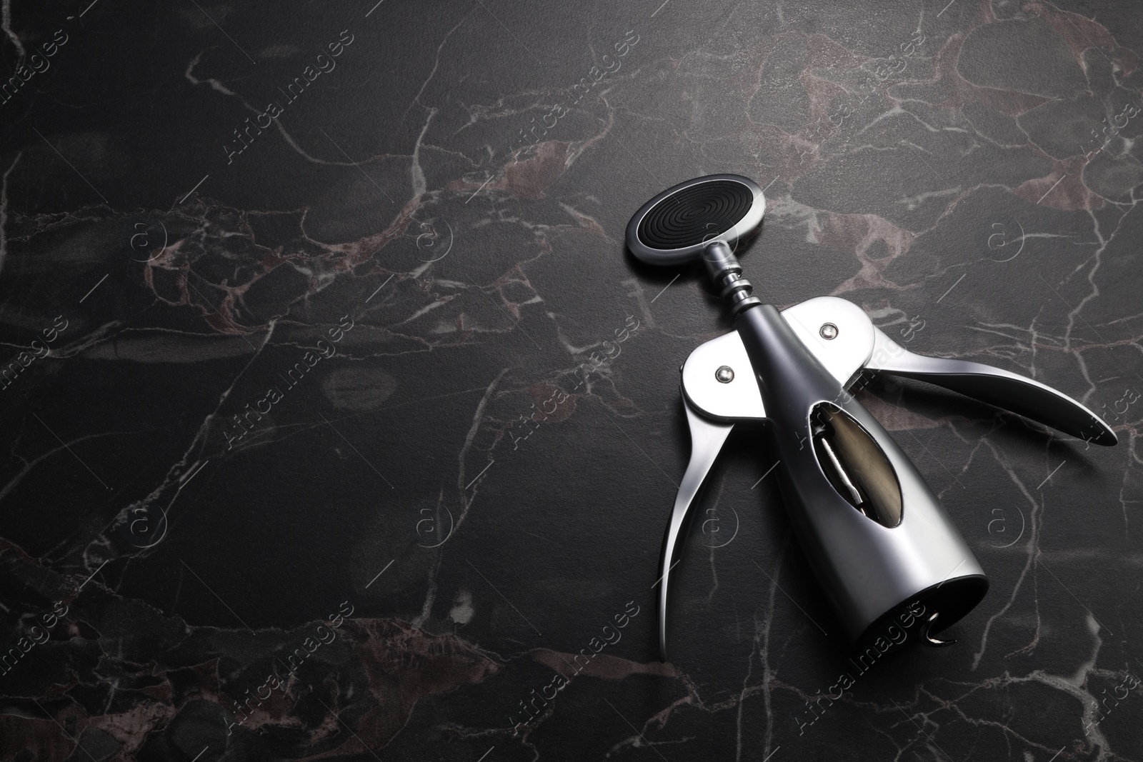 Photo of One wing corkscrew on black marble table. Space for text