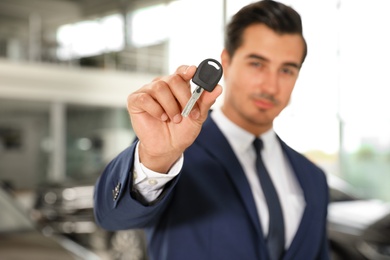 Young salesman with car key in modern dealership, focus on hand