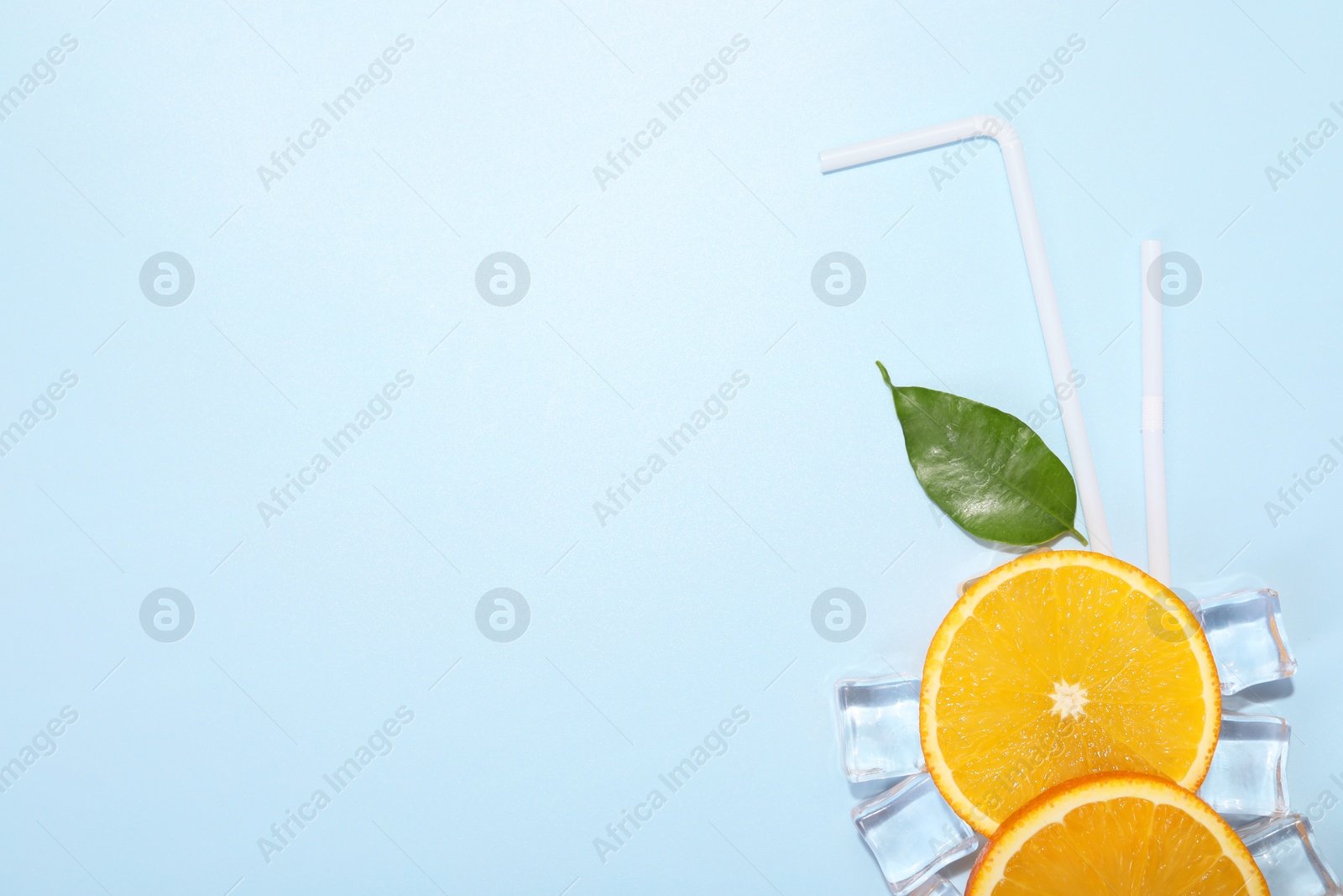 Photo of Slices of juicy orange, ice cubes and leaf on light blue background, flat lay. Space for text