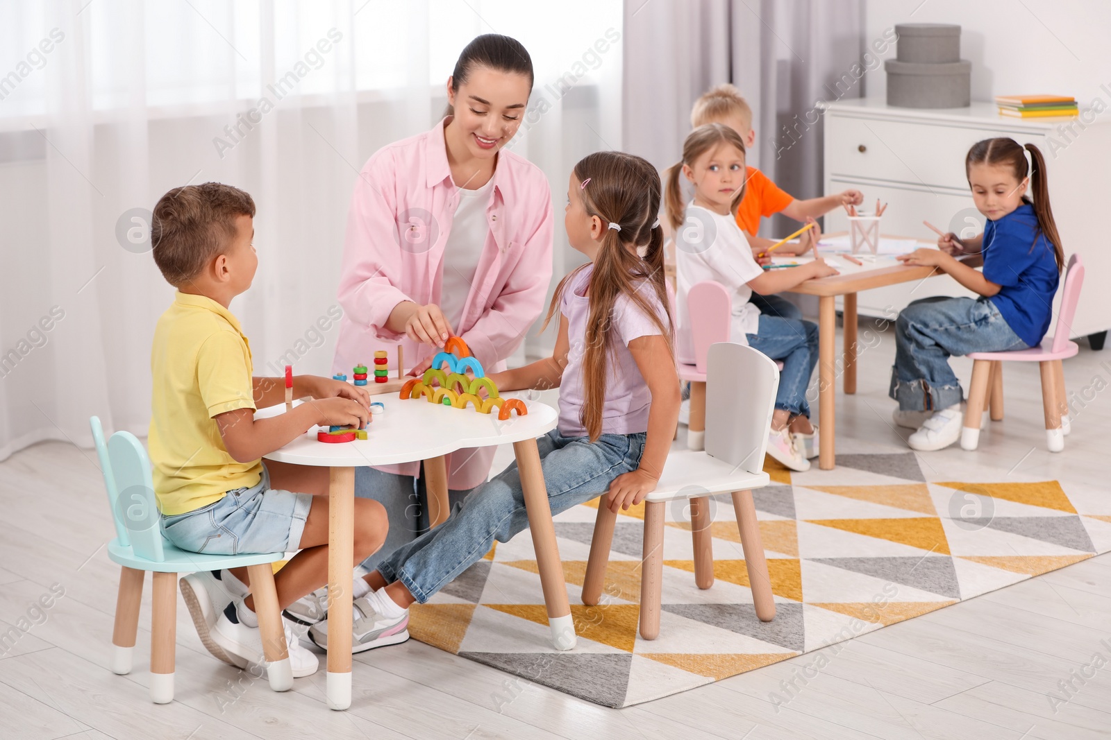 Photo of Nursery teacher and group of cute little children playing at desks in kindergarten. Activities for motor skills development