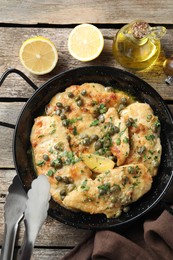 Delicious chicken piccata with herbs and lemon on wooden table, flat lay