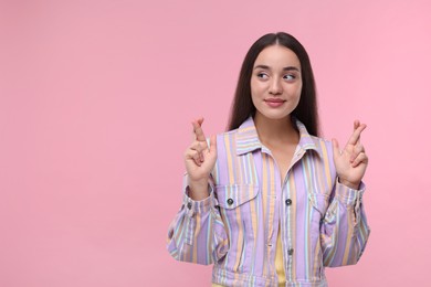 Photo of Happy woman crossing her fingers on pink background, space for text