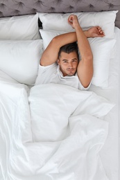 Photo of Young man lying in bed with soft pillows at home, top view