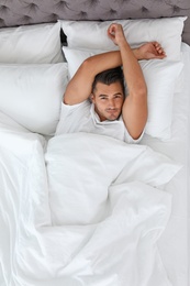 Young man lying in bed with soft pillows at home, top view