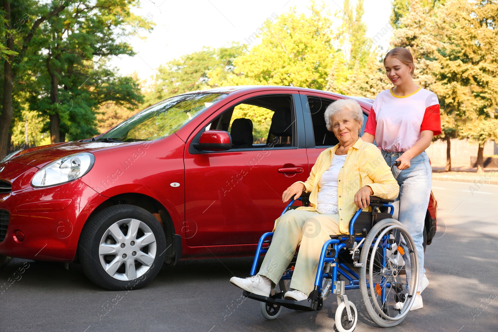 Photo of Senior woman in wheelchair with granddaughter near car outdoors