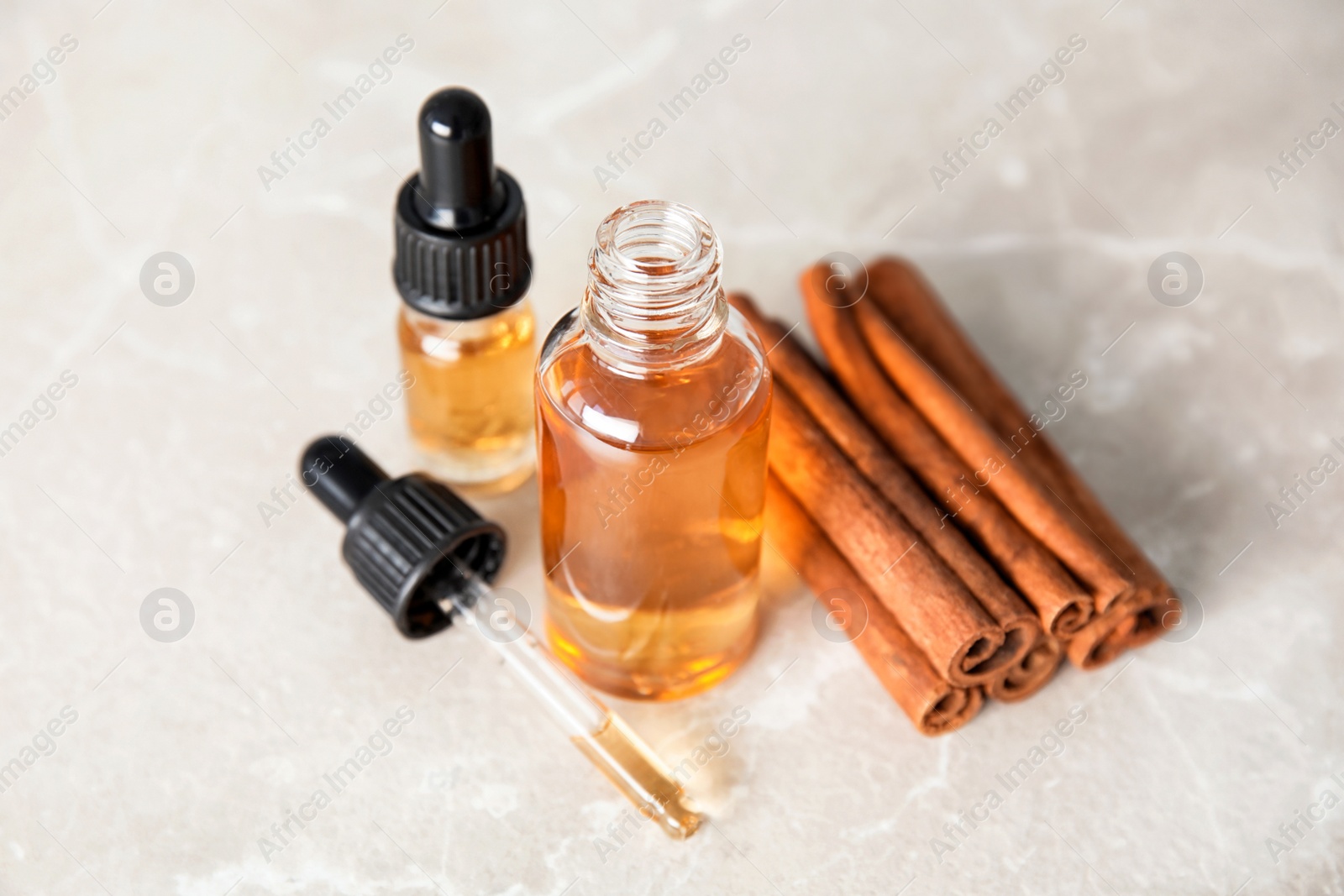 Photo of Bottles of essential oils and cinnamon sticks on grey marble table