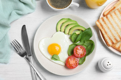 Photo of Tasty breakfast with heart shaped fried egg served on white wooden table, flat lay