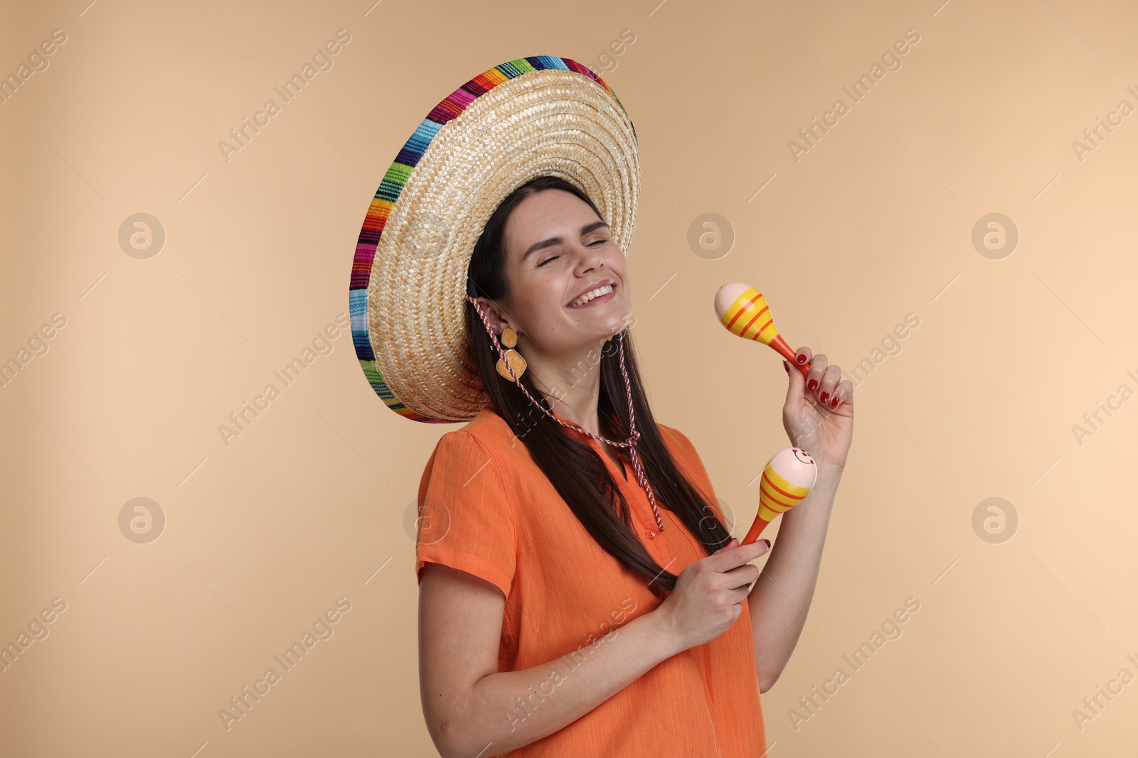 Photo of Young woman in Mexican sombrero hat with maracas on beige background