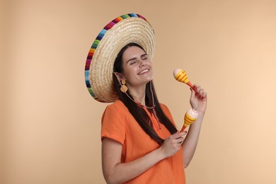 Young woman in Mexican sombrero hat with maracas on beige background