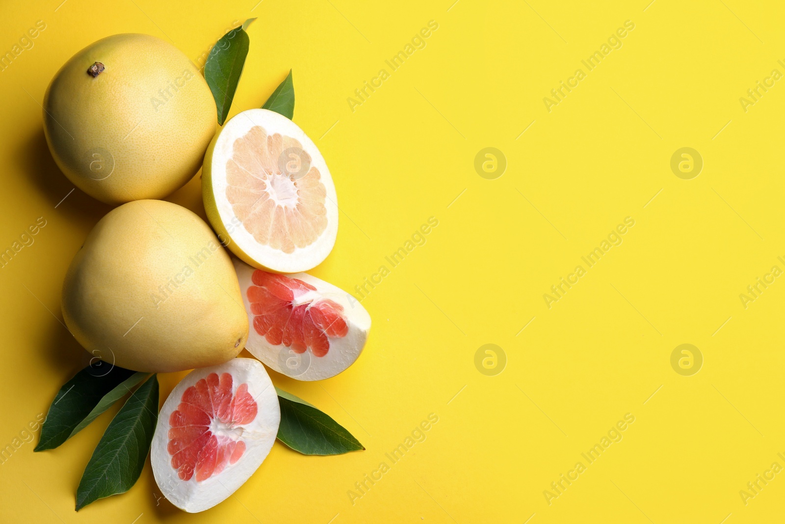 Photo of Fresh cut and whole pomelo fruits with leaves on yellow background, flat lay. Space for text