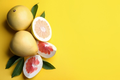 Photo of Fresh cut and whole pomelo fruits with leaves on yellow background, flat lay. Space for text