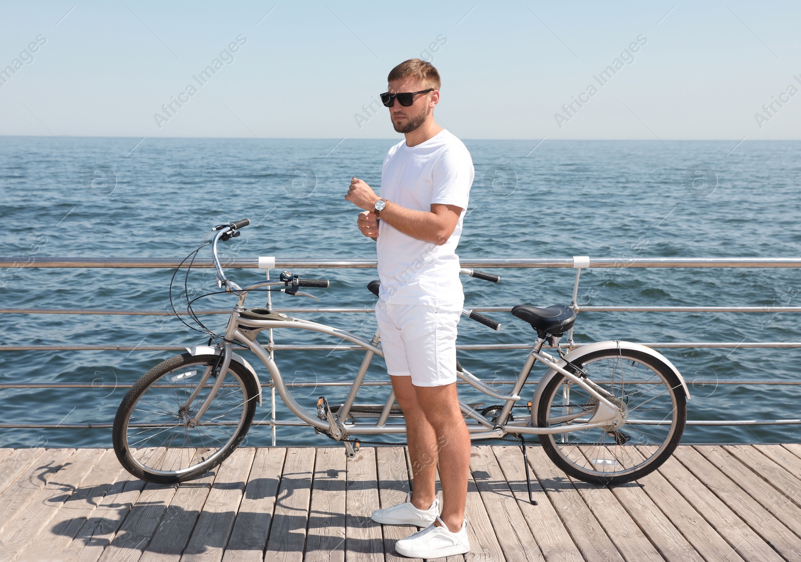 Photo of Attractive man with tandem bike near sea on sunny day