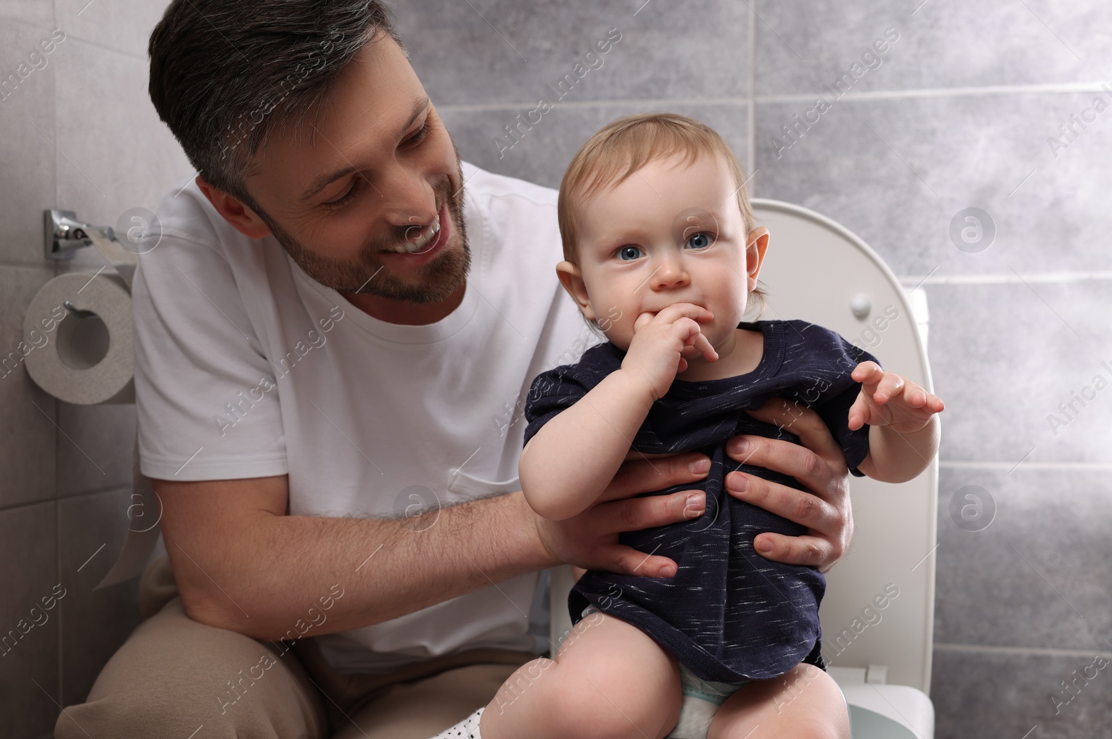 Photo of Father training his child to sit on toilet bowl indoors