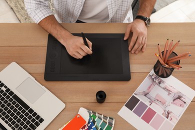 Professional designer with graphic tablet at wooden table, closeup