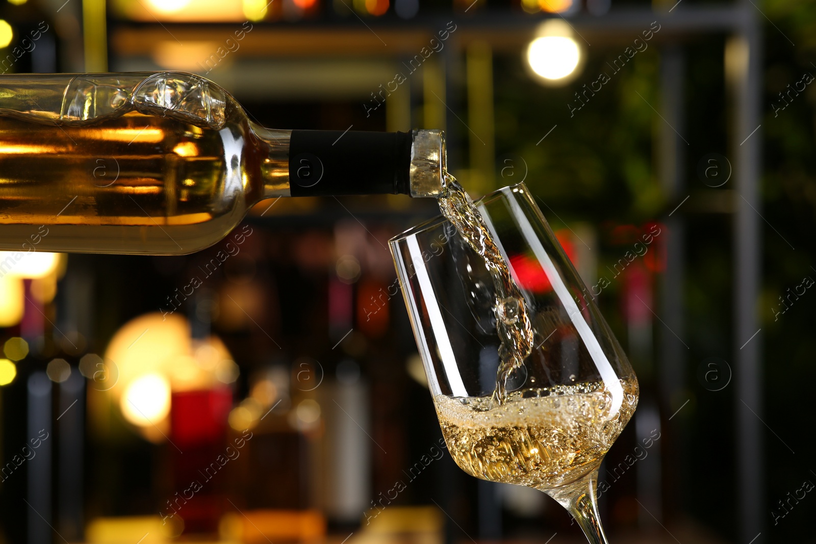 Photo of Pouring white wine from bottle into glass on blurred background, closeup