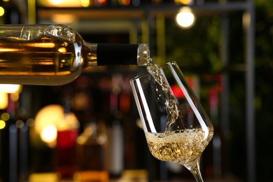 Photo of Pouring white wine from bottle into glass on blurred background, closeup