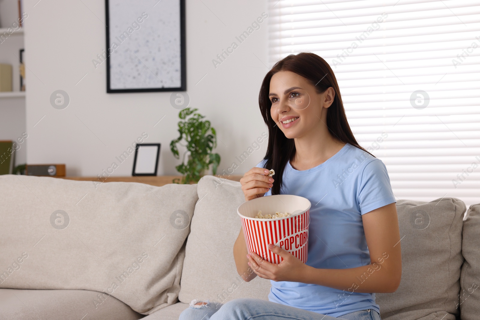 Photo of Happy woman with popcorn bucket watching TV on sofa at home