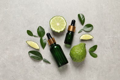 Photo of Glass bottles of bergamot essential oil and fresh fruits on light table, flat lay