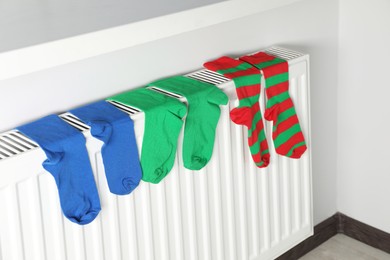 Photo of Different colorful socks hanging on white radiator indoors