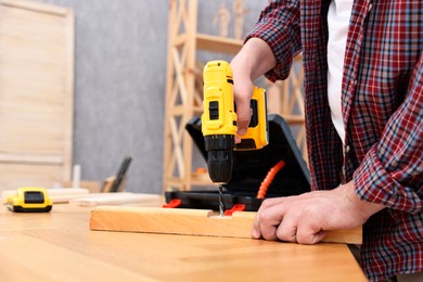 Photo of Young handyman working with electric drill at table in workshop, closeup