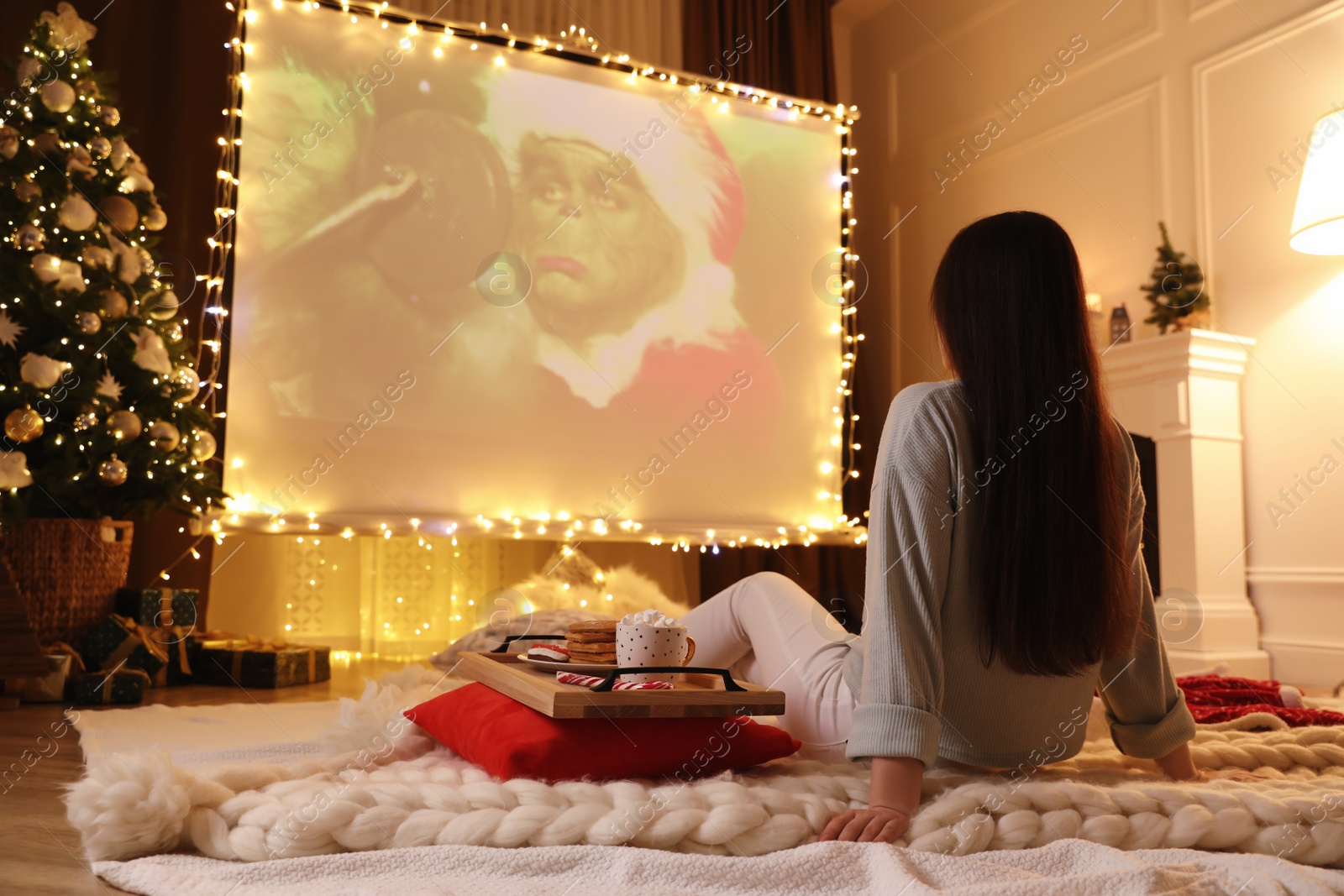 Photo of MYKOLAIV, UKRAINE - DECEMBER 24, 2020: Woman watching The Grinch movie via video projector in room. Cozy winter holidays atmosphere