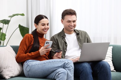 Photo of Happy couple with credit card and gadgets shopping online together at home