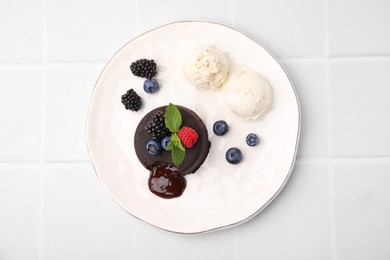 Plate with delicious chocolate fondant, berries, ice cream and mint on white tiled table, top view