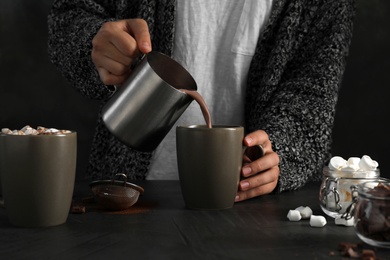 Photo of Woman pouring hot chocolate with milk into cup on table, closeup