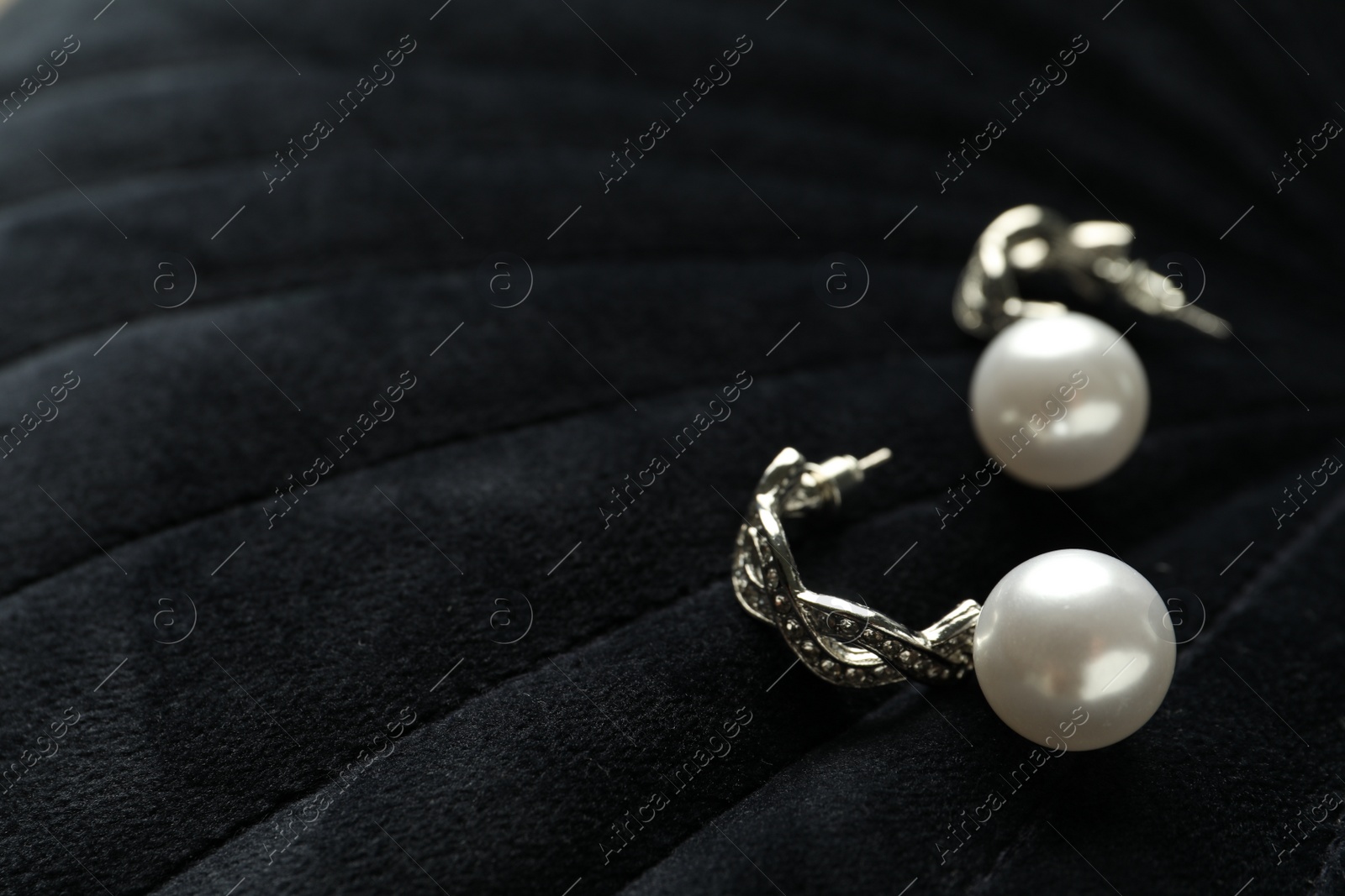 Photo of Elegant silver earrings with pearls on black fabric, closeup. Space for text