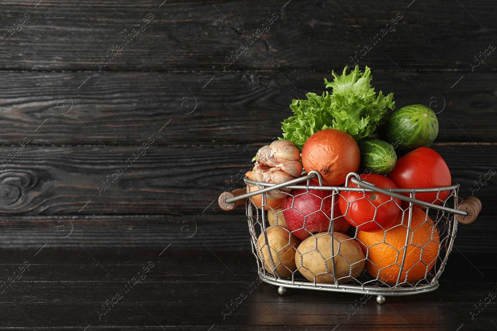 Photo of Basket with ripe fruits and vegetables on black table. Space for text