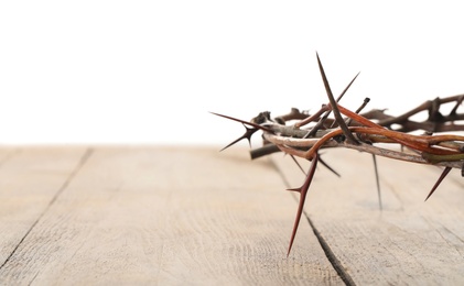 Photo of Crown of thorns on wooden table against white background, closeup with space for text. Easter attribute