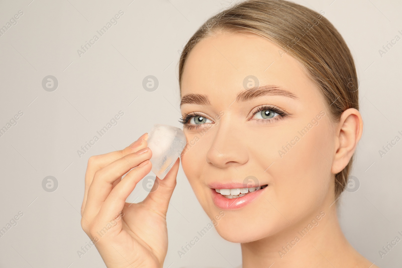 Photo of Young woman with ice cube on light background. Skin care