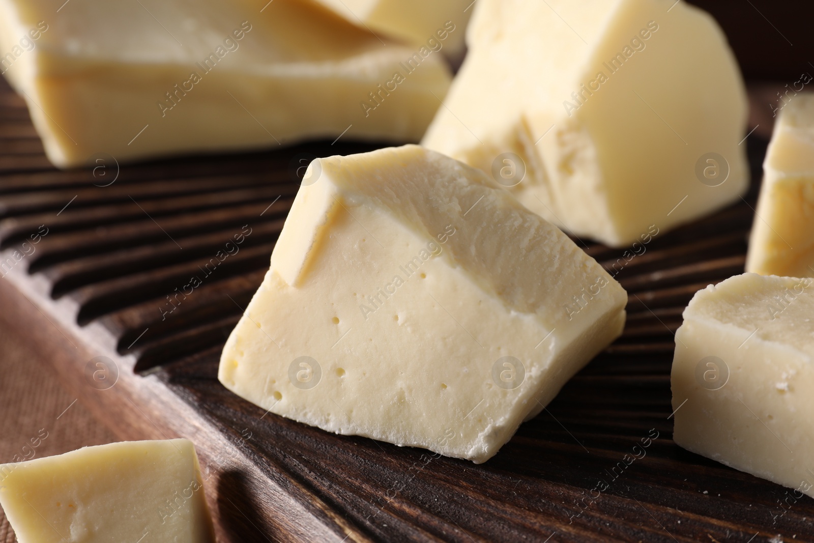 Photo of Pieces of tasty white chocolate on wooden board, closeup