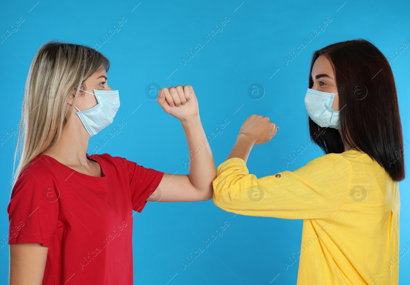 Photo of Women bumping elbows to say hello on light blue background. Keeping social distance during coronavirus pandemic