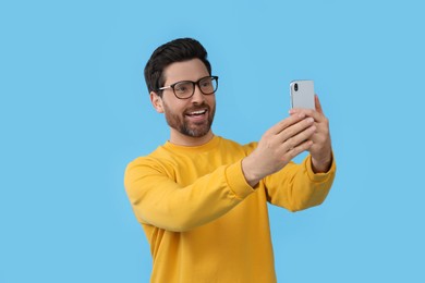 Smiling man taking selfie with smartphone on light blue background