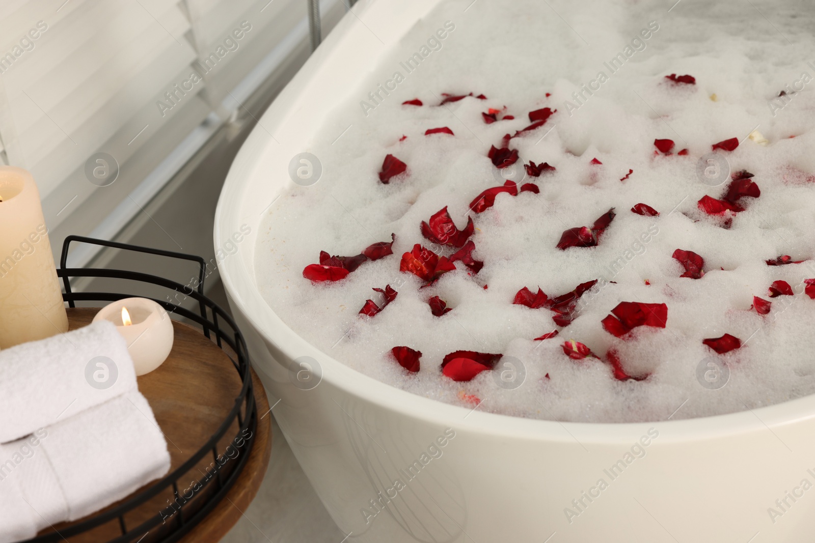 Photo of Bath tub with foam and red rose petals in bathroom