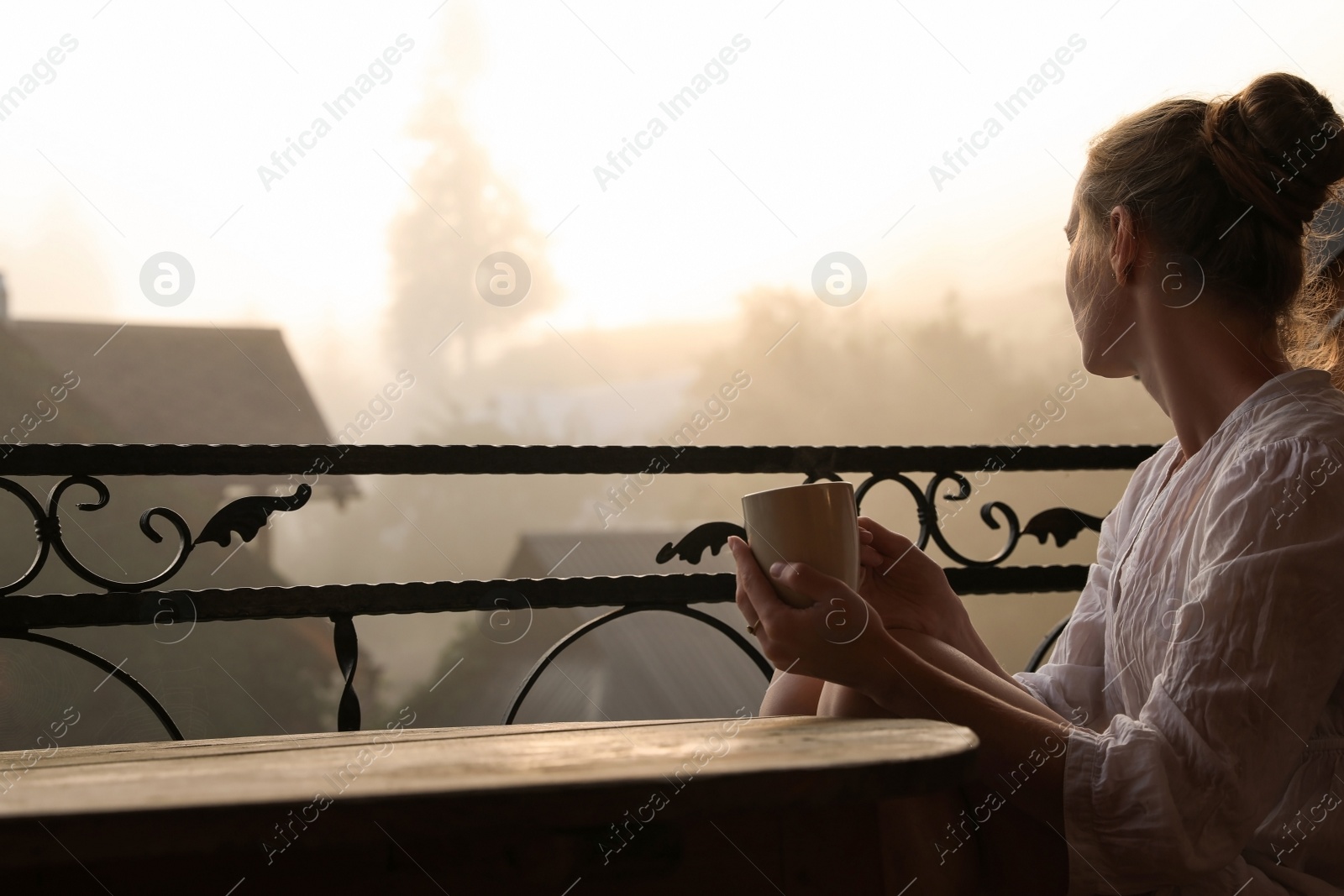 Photo of Young woman sitting at table on balcony with cup of tea in morning