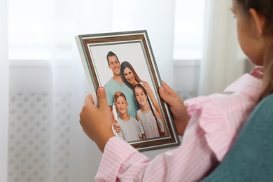 Photo of Little girl holding framed family photo indoors, closeup