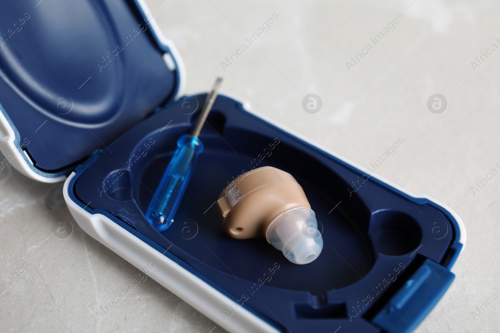 Photo of Case with hearing aid and small screwdriver on grey background, closeup