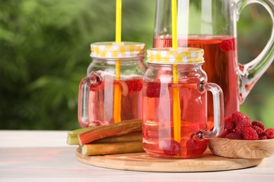 Photo of Tasty rhubarb cocktail with raspberry and stalks on white wooden table outdoors