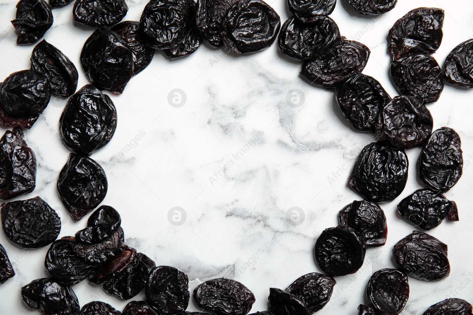 Photo of Frame of sweet dried plums on marble background, top view with space for text. Healthy fruit