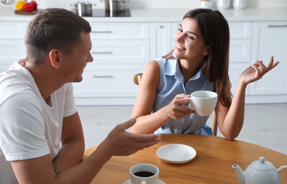 Photo of Man and woman talking while drinking tea at table in kitchen