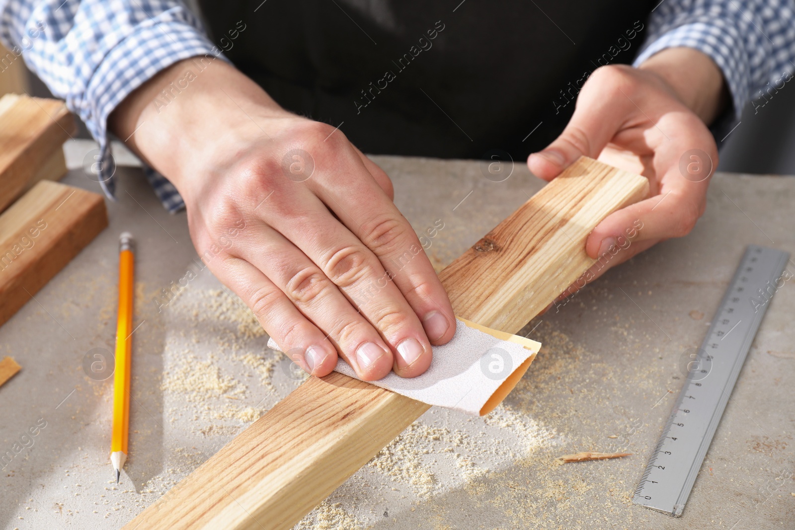 Photo of Man polishing wooden plank with sandpaper at grey table, closeup