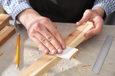 Man polishing wooden plank with sandpaper at grey table, closeup