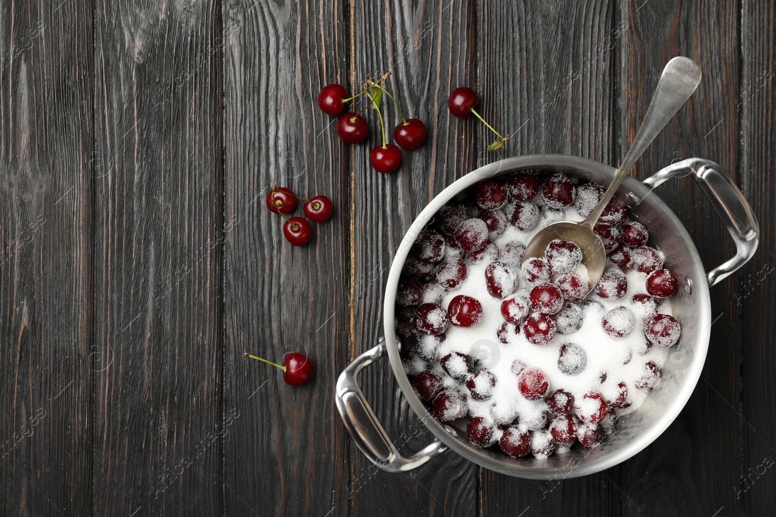Photo of Pot with cherries and sugar on black wooden table, flat lay. Making of delicious jam