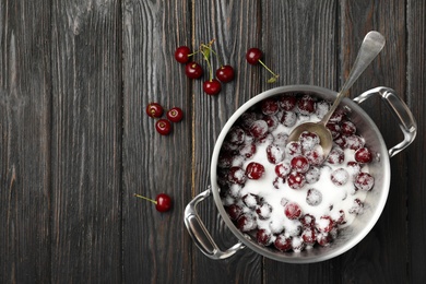 Pot with cherries and sugar on black wooden table, flat lay. Making of delicious jam
